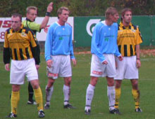 Dommeren med to fingre i vejret, omgivet af spillere (foto: T. Brygger)